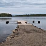 Puinen pitkä laituri jossa puomeja. Laituri on järvessä. Järvi on sininen. Laituri on puinen.